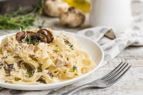 Pasta fettuccine with mushrooms and fried chicken ham in creamy cheese sauce on a light wooden background